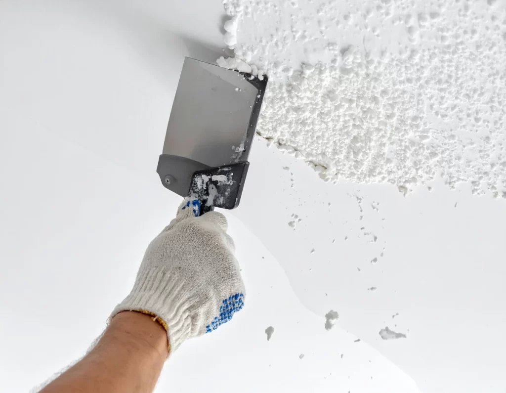 DIYer scraping popcorn ceiling texture off using a putty knife